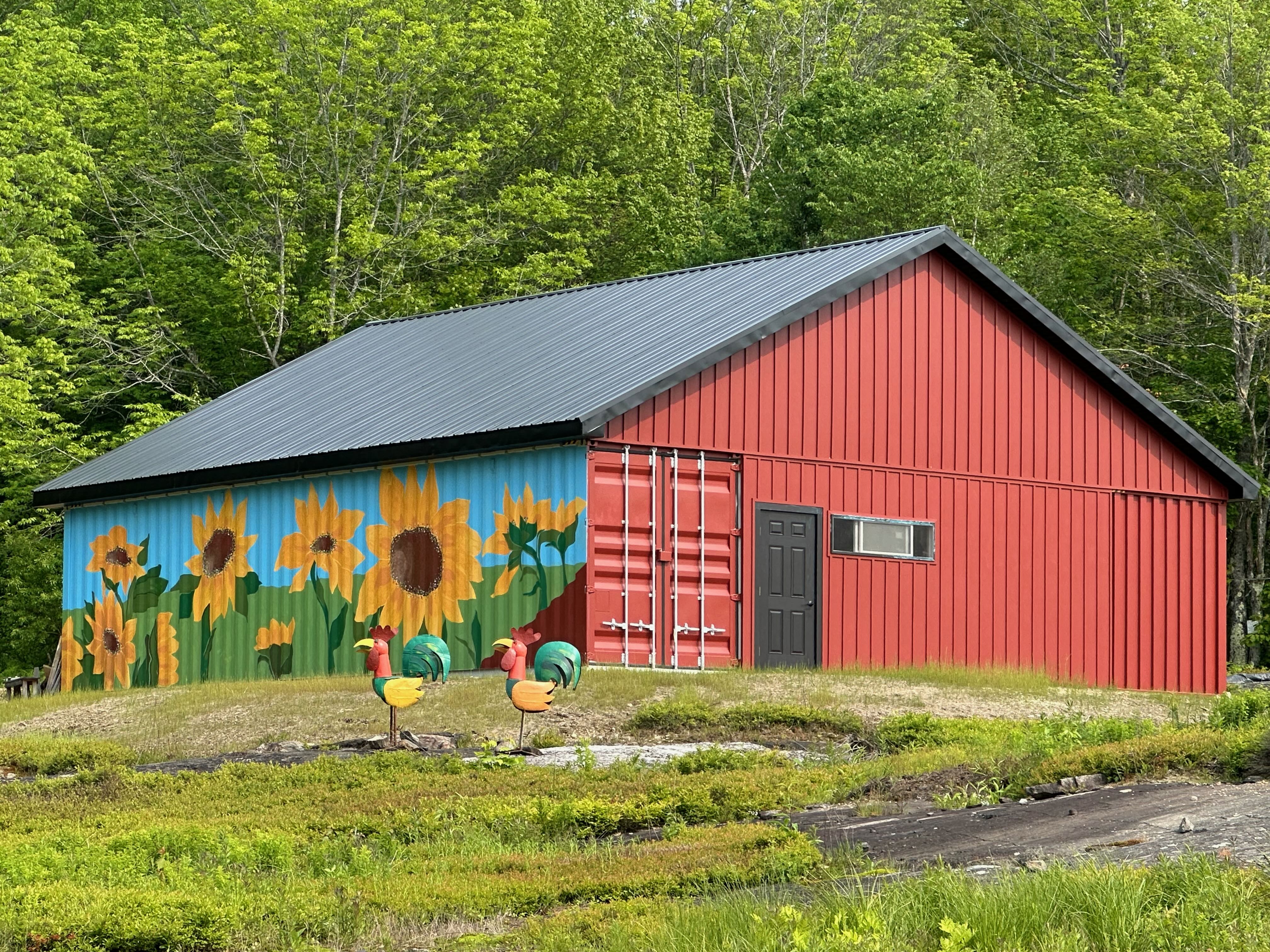 Red tractor barn with a sunflower mural and metal rooster sculptures